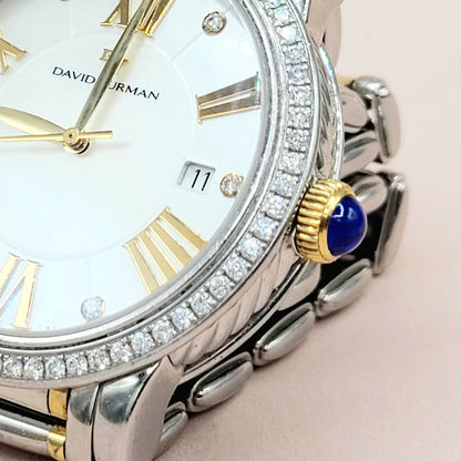 Luxury watch with diamond-studded bezel and blue gemstone on a light pink background