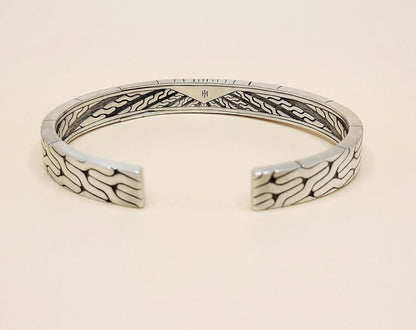 A sterling silver cuff bracelet with intricate engraved wave patterns on the exterior and interior, displayed on a light beige background.