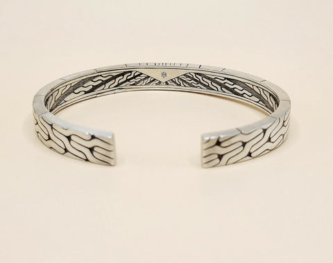 A sterling silver cuff bracelet with intricate engraved wave patterns on the exterior and interior, displayed on a light beige background.