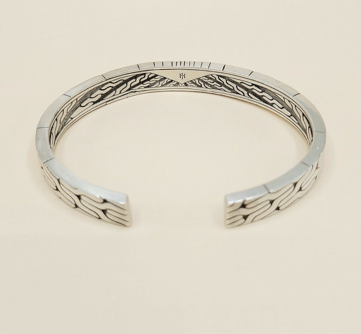 A sterling silver cuff bracelet with a textured, geometric wave pattern on the outer surface and a polished inner band, shown on a light beige background.