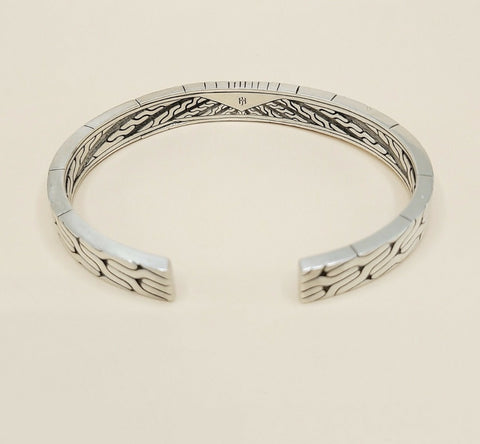 A sterling silver cuff bracelet with a textured, geometric wave pattern on the outer surface and a polished inner band, shown on a light beige background.