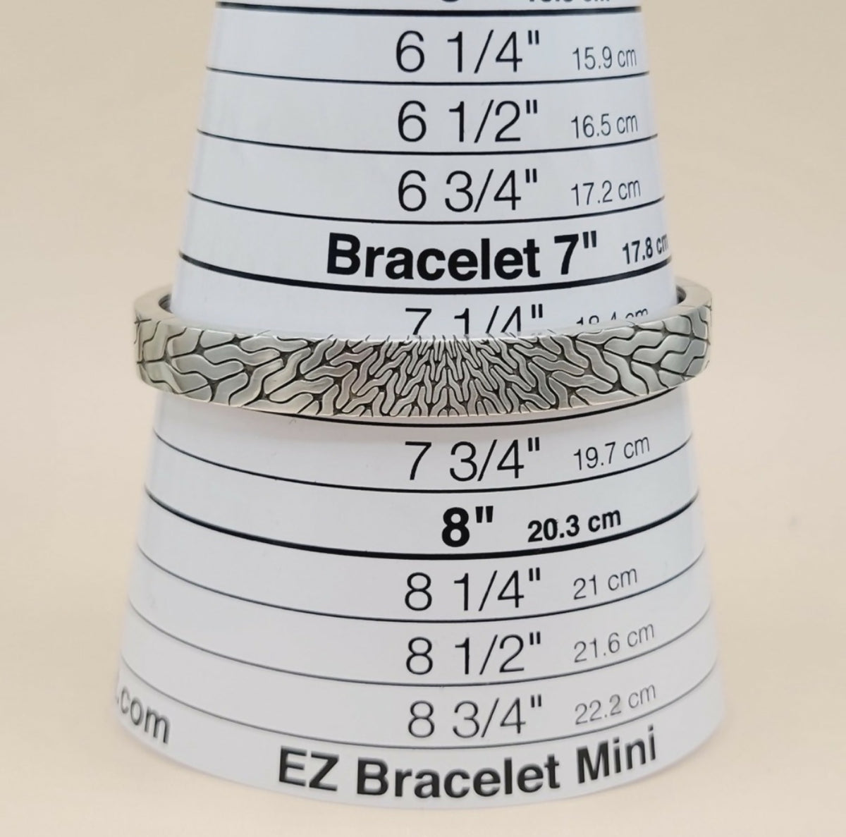 A silver bracelet with a textured, wavy patterned design, displayed on a white cone-shaped sizing tool labeled 'EZ Bracelet Mini'.