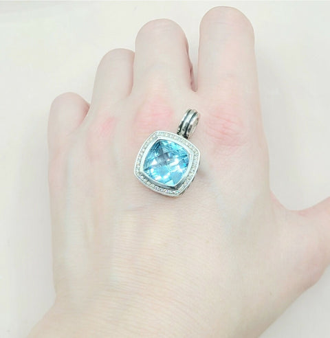 Blue gemstone pendant held in a hand against a white background