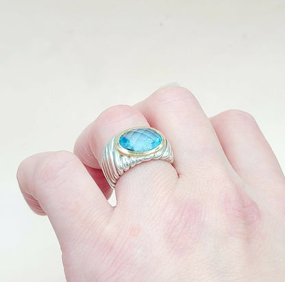 Hand wearing a ring with a blue gemstone on a light background
